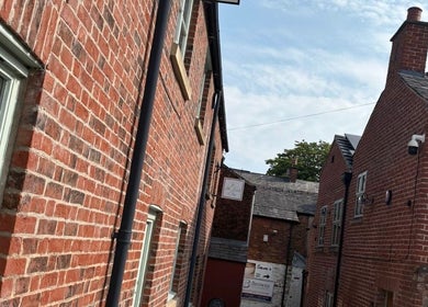 Charming brick alleyway leading to Sculpt & Pout SPMU in Congleton, England, GB, with blue sky overhead.
