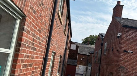 Charming brick alleyway leading to Sculpt & Pout SPMU in Congleton, England, GB, with blue sky overhead.