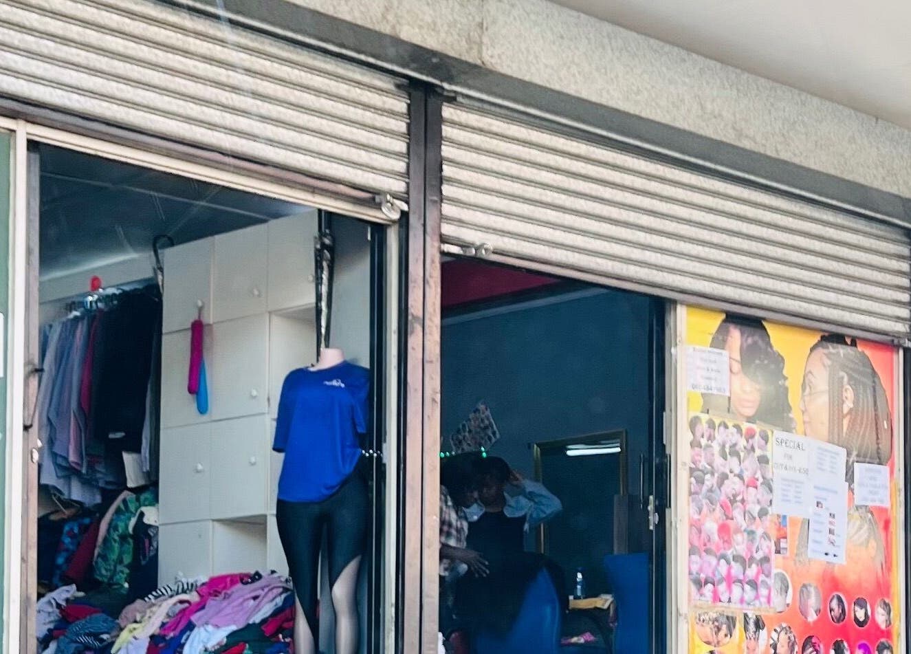 Entrance of Nail’d By Mash in Emalahleni, Mpumalanga, ZA, showcasing colorful clothing and hairstyle posters.