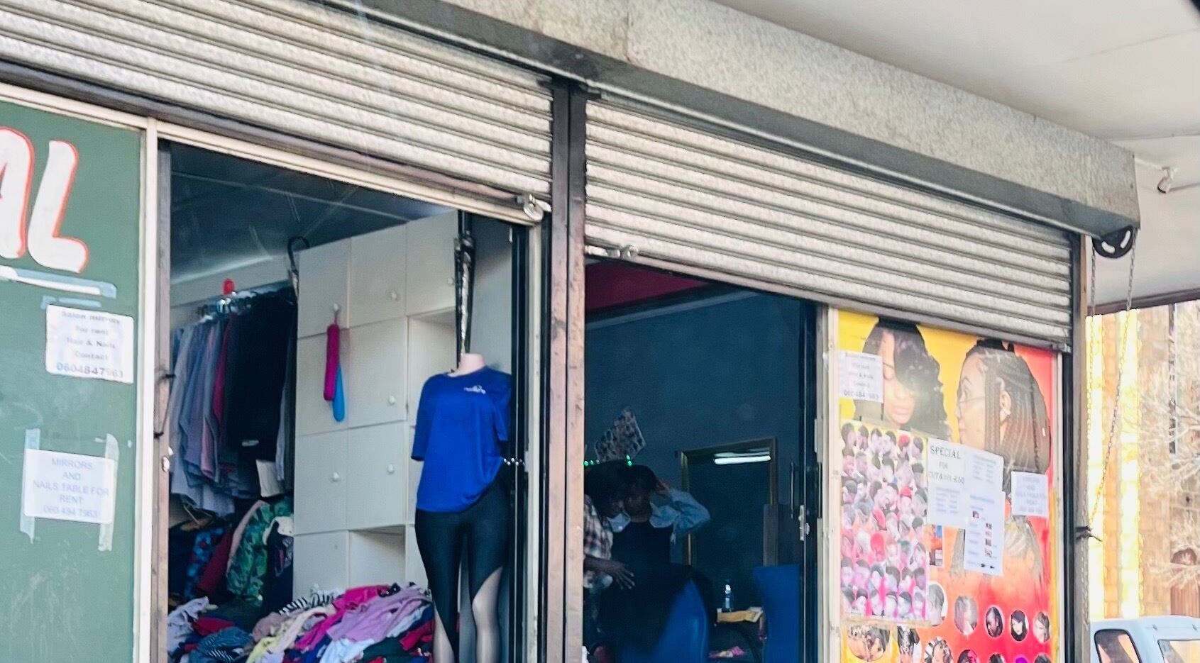 Entrance of Nail’d By Mash in Emalahleni, Mpumalanga, ZA, showcasing colorful clothing and hairstyle posters.