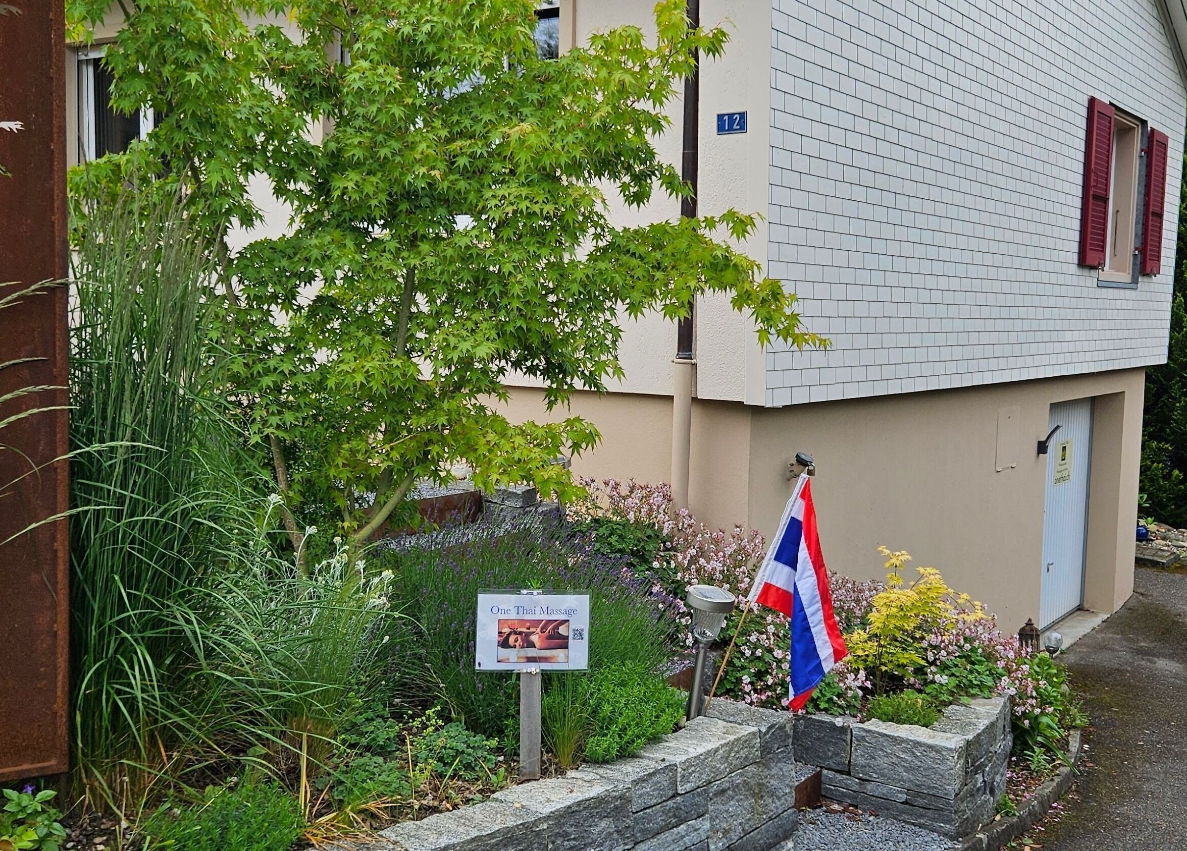 Eingang von One Thai Massage Ipsach, umgeben von üppigem Grün in Ipsach, Bern, CH.