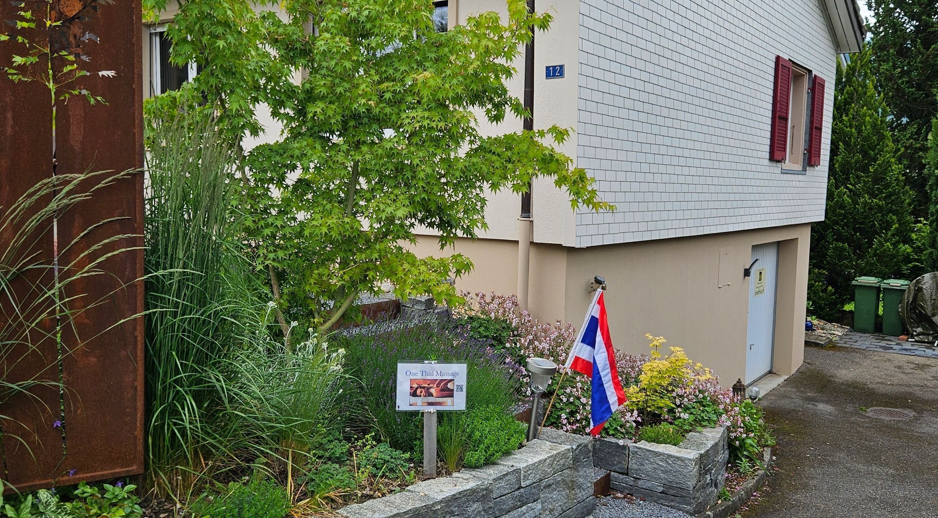 Eingang von One Thai Massage Ipsach, umgeben von üppigem Grün in Ipsach, Bern, CH.