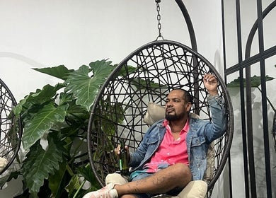 Hombre relajado en silla colgante en Nua 360 Spa Piura, Piura, Piura, PE, rodeado de plantas verdes.