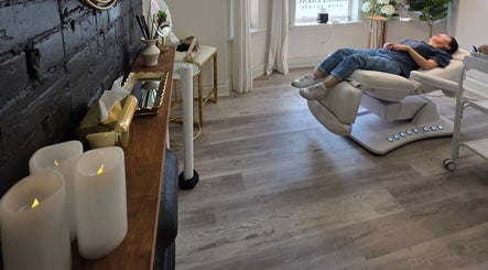 Client relaxing on a modern chair at Beauty by Bahar, Toronto, Ontario, CA, with candles and chic decor.