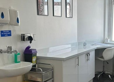 A clean, modern treatment room at Simply Glow Aesthetics, Bathgate, Scotland, GB with white cabinetry and handwash sink.