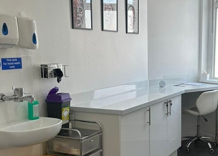 A clean, modern treatment room at Simply Glow Aesthetics, Bathgate, Scotland, GB with white cabinetry and handwash sink.