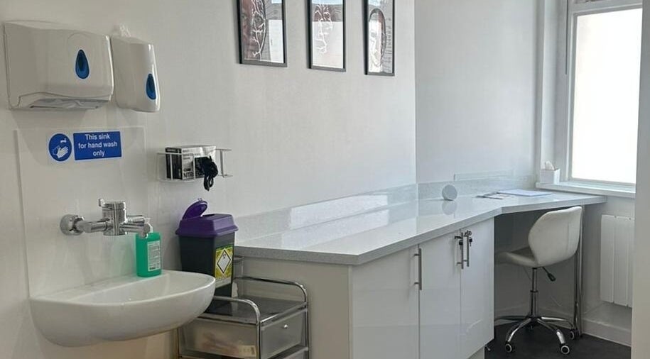 A clean, modern treatment room at Simply Glow Aesthetics, Bathgate, Scotland, GB with white cabinetry and handwash sink.