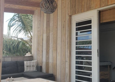 Rustieke houten veranda bij Voetreflextherapie Bonaire, Nikiboko, omgeven door palmbomen.