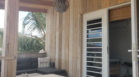 Rustieke houten veranda bij Voetreflextherapie Bonaire, Nikiboko, omgeven door palmbomen.
