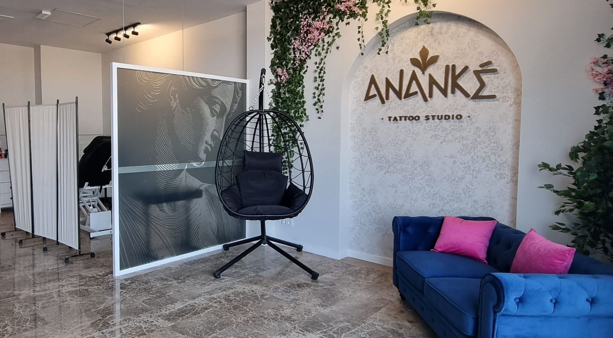 Interior moderno de Ananké Tattoo Studio en Sedaví, Comunidad Valenciana, ES con sofá azul y silla colgante.