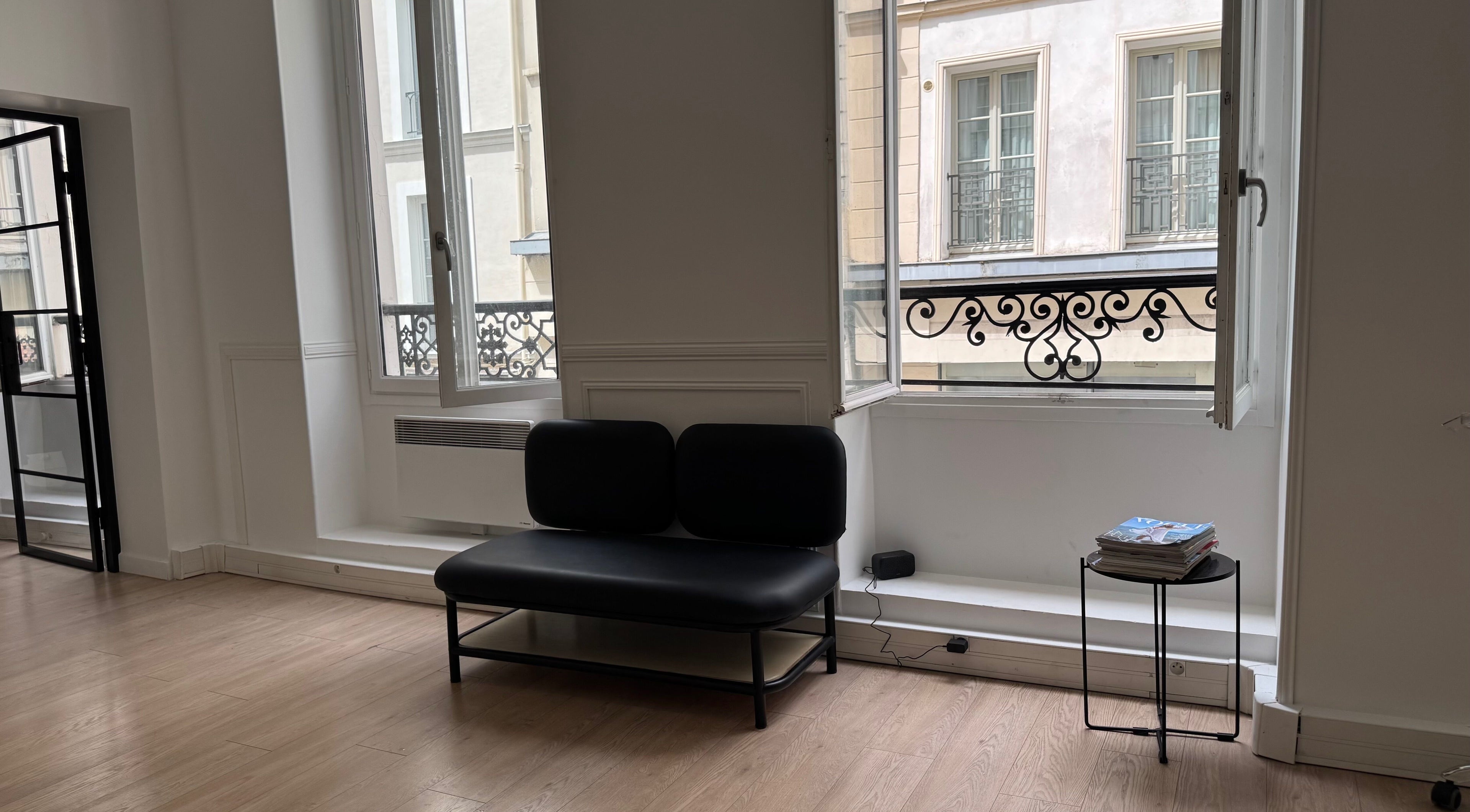 Intérieur moderne de Leonard à Paris, Île-de-France, FR avec canapé noir et fenêtres lumineuses.