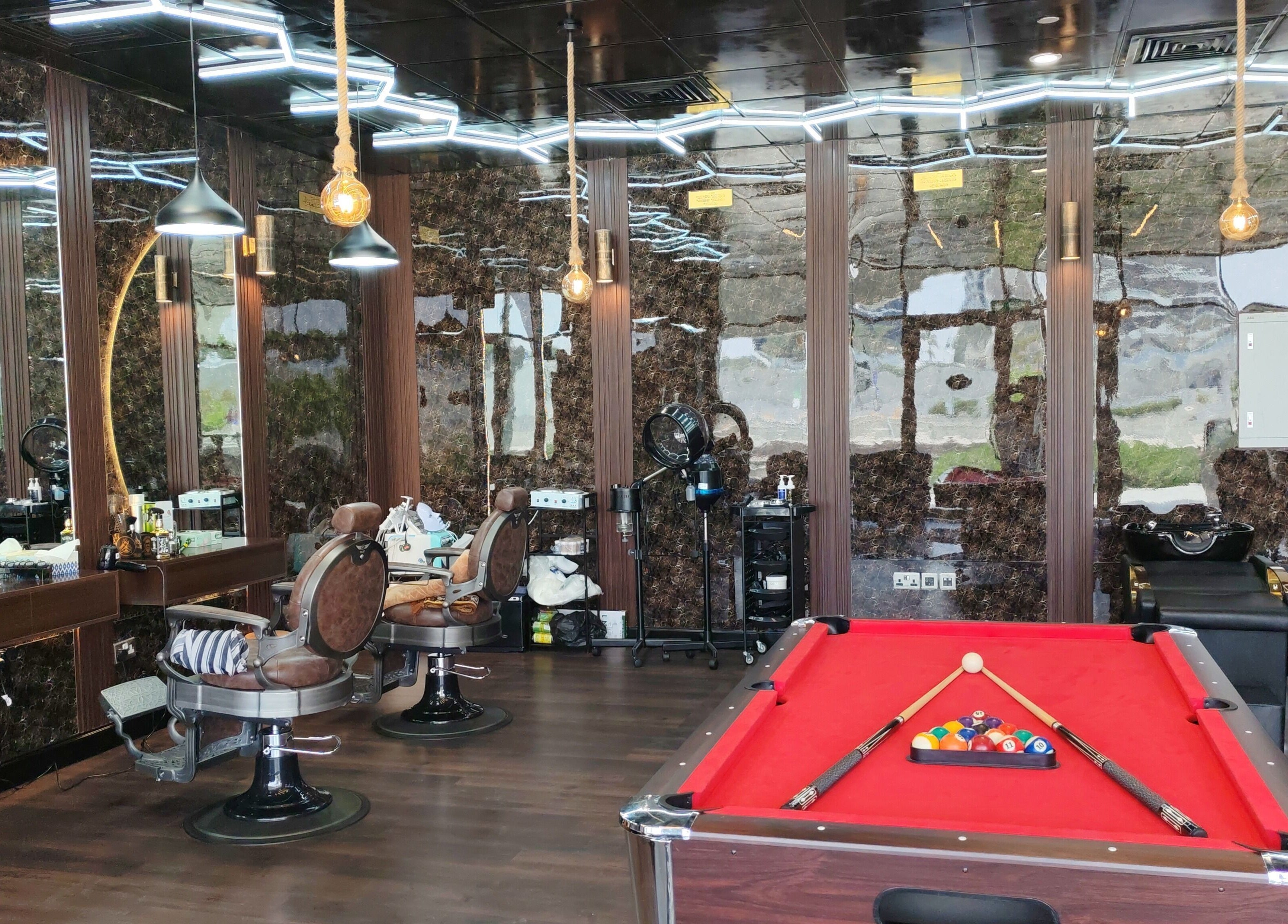 مشهد داخلي لصالون Les Messieurs في أبو ظبي يتضمن كراسي حلاقة وطاولة بلياردو.