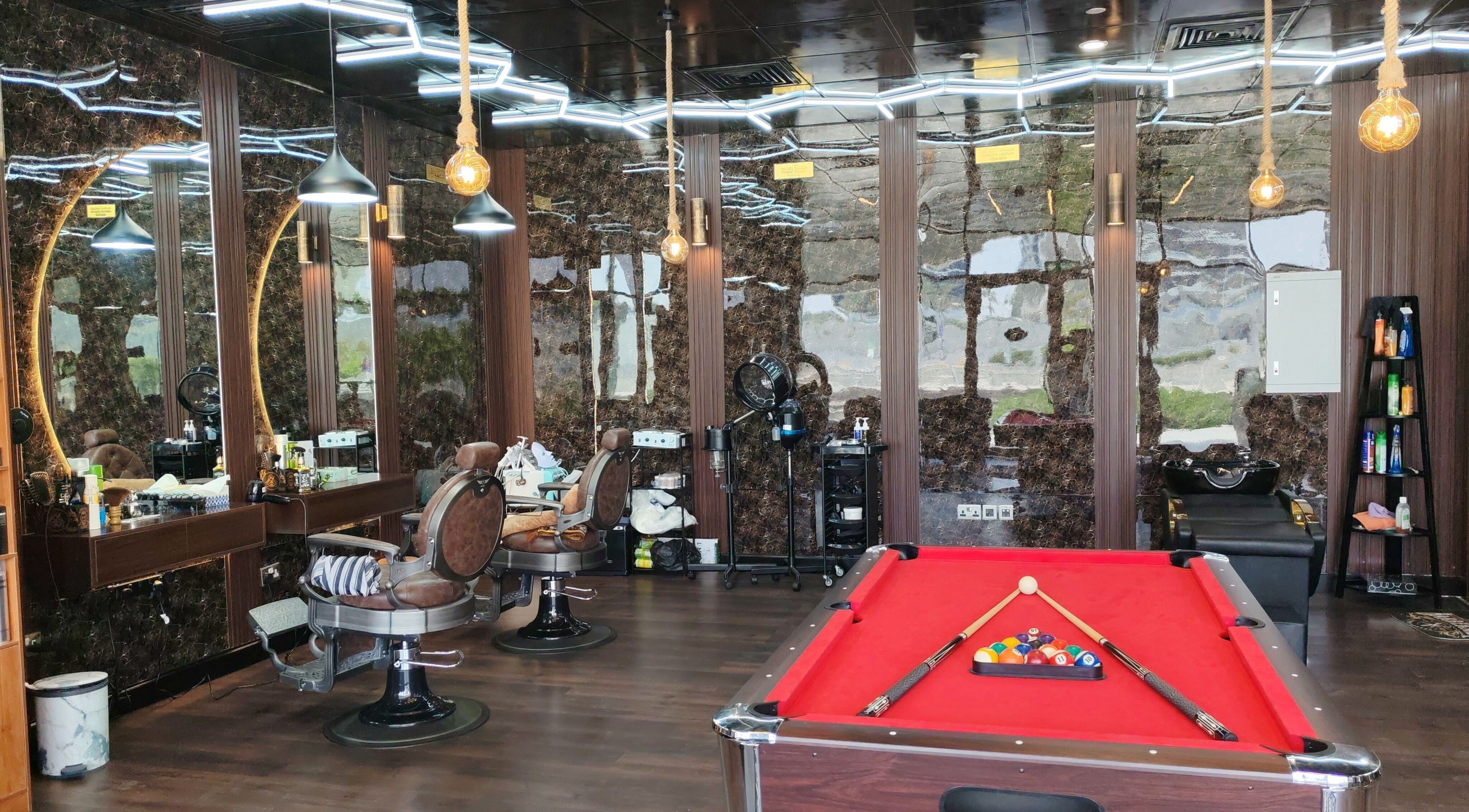 مشهد داخلي لصالون Les Messieurs في أبو ظبي يتضمن كراسي حلاقة وطاولة بلياردو.