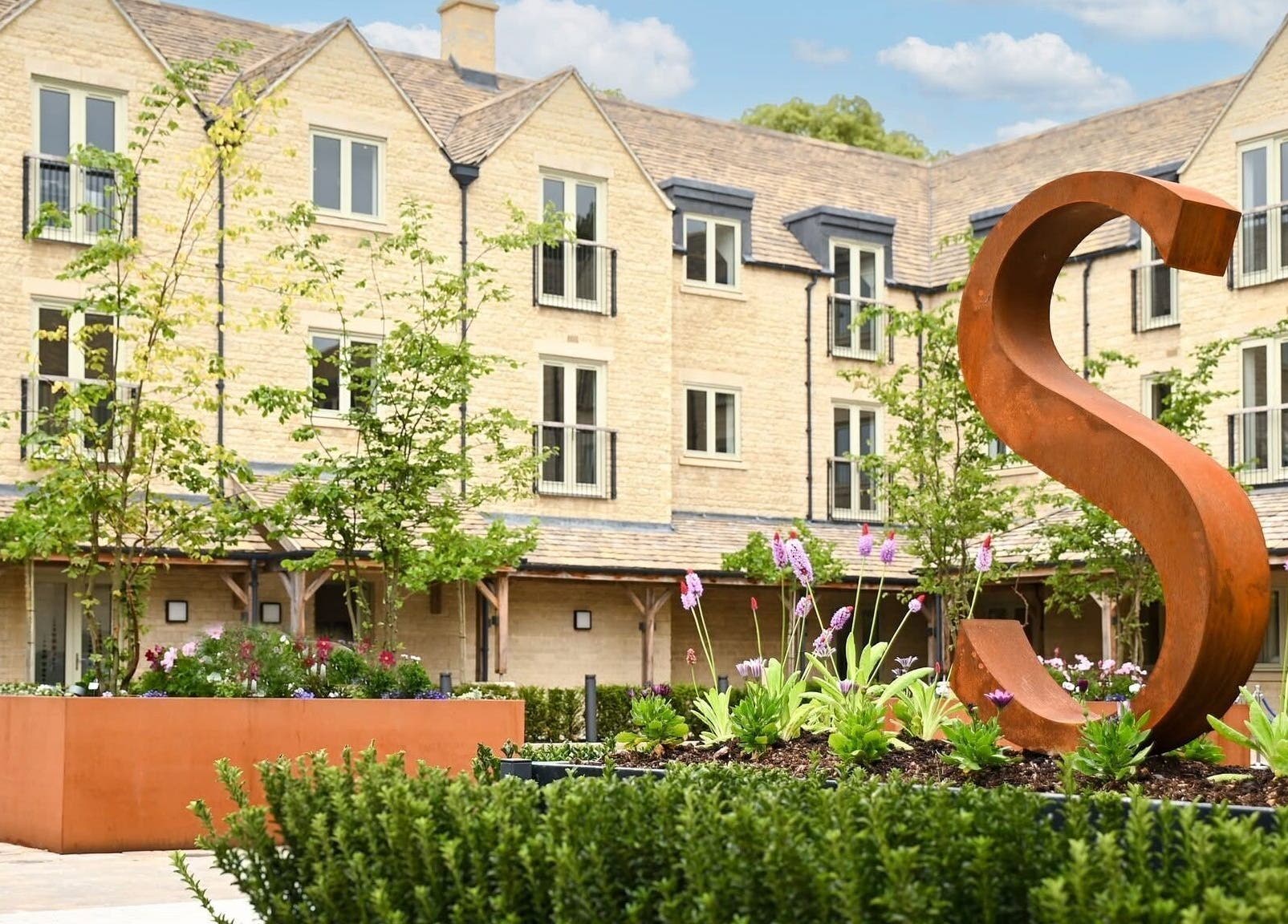 Charming courtyard at Reflex Harmony, Cirencester, England, GB with modern sculpture and lush greenery.