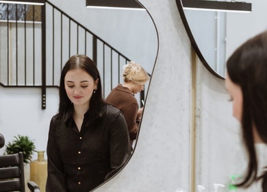 Woman at Drader Brows salon mirror, Auckland, Auckland, NZ, reflecting modern elegance.