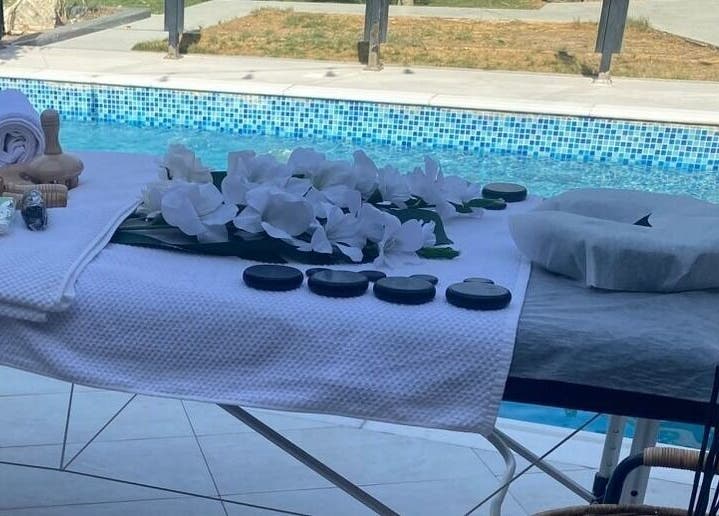 Massage table by pool at MMSPA - Home Service, Riyadh, SA, with towels and stones for relaxation.