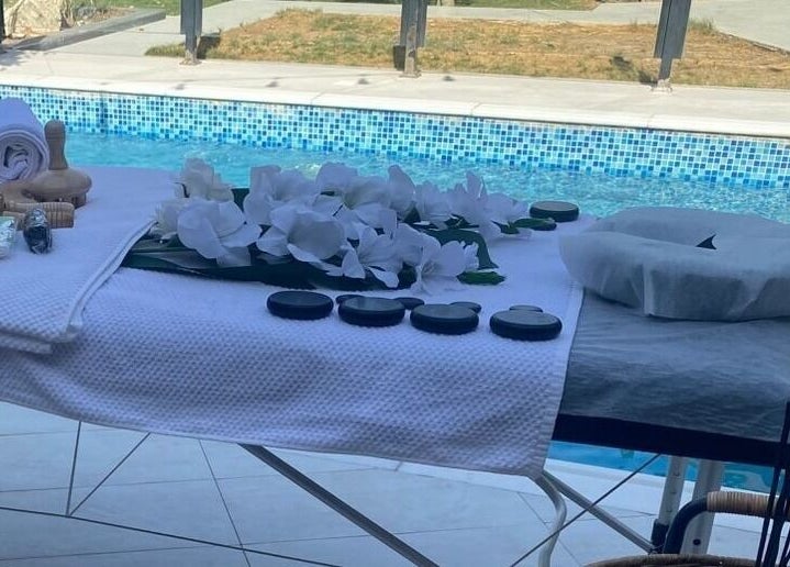Massage table by pool at MMSPA - Home Service, Riyadh, SA, with towels and stones for relaxation.