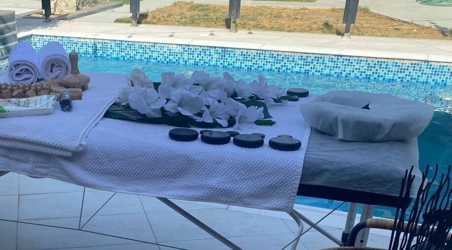 Massage table by pool at MMSPA - Home Service, Riyadh, SA, with towels and stones for relaxation.