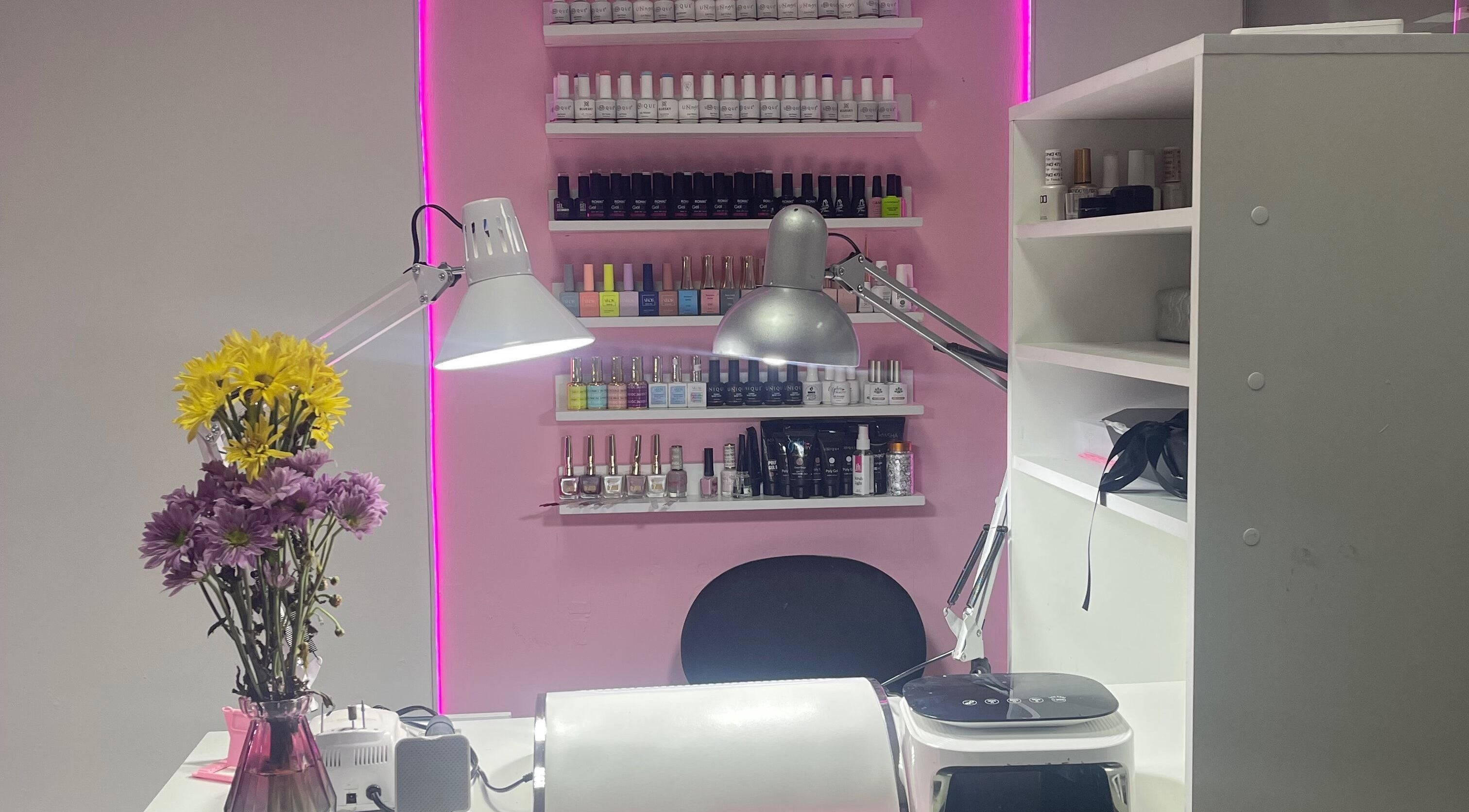 Mesa de manicura en Lili Glam Nails, Panamá City, con esmaltes y flores sobre fondo rosado.