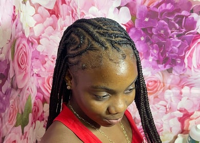 Intricate braids at Tressed By Jai, Roseau, Saint George Parish, DM, with a floral backdrop.