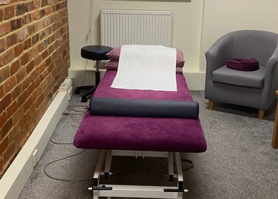 Cozy treatment room at Matter of Clarity, Finchampstead, England, GB with purple massage table and gray chair.