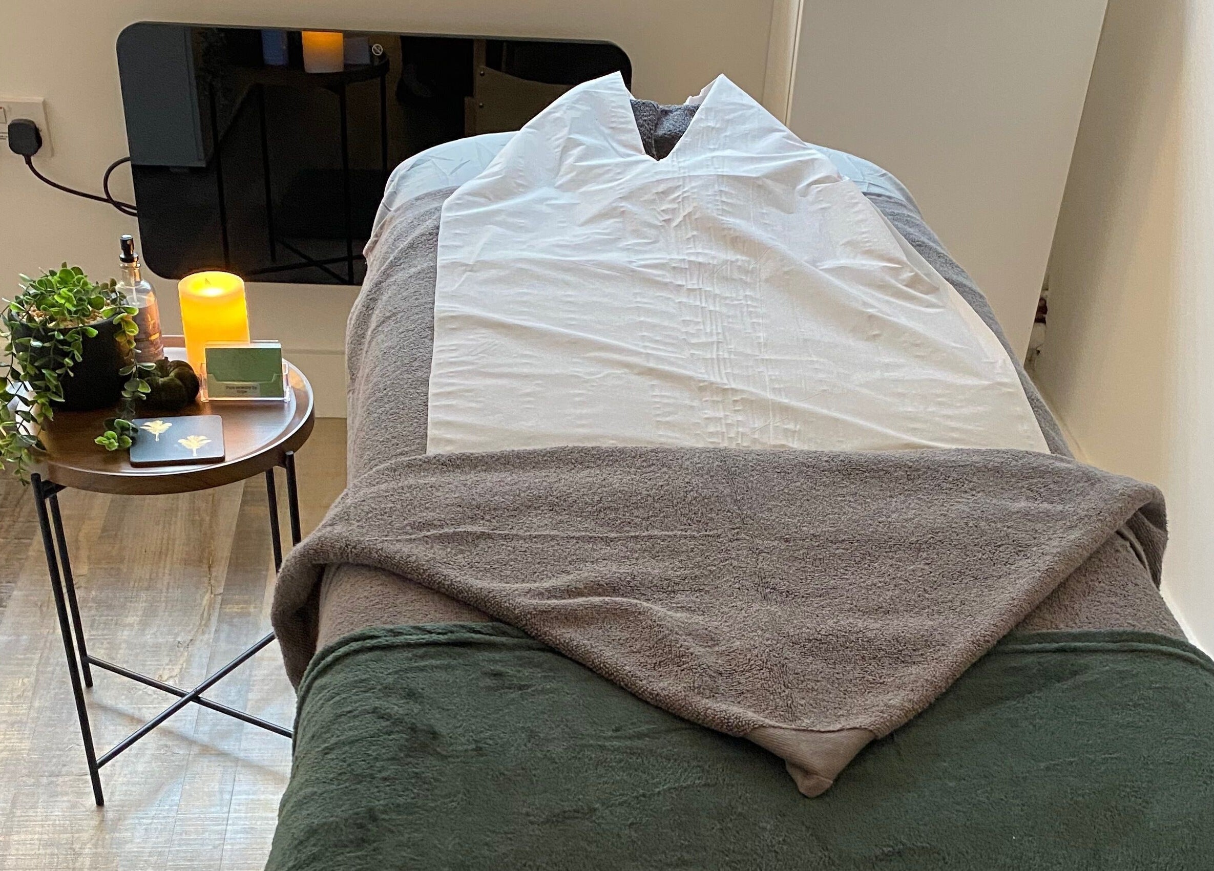 Massage table setup at Pure Serenity By Hope in Norwich, England, GB with candles and greenery.