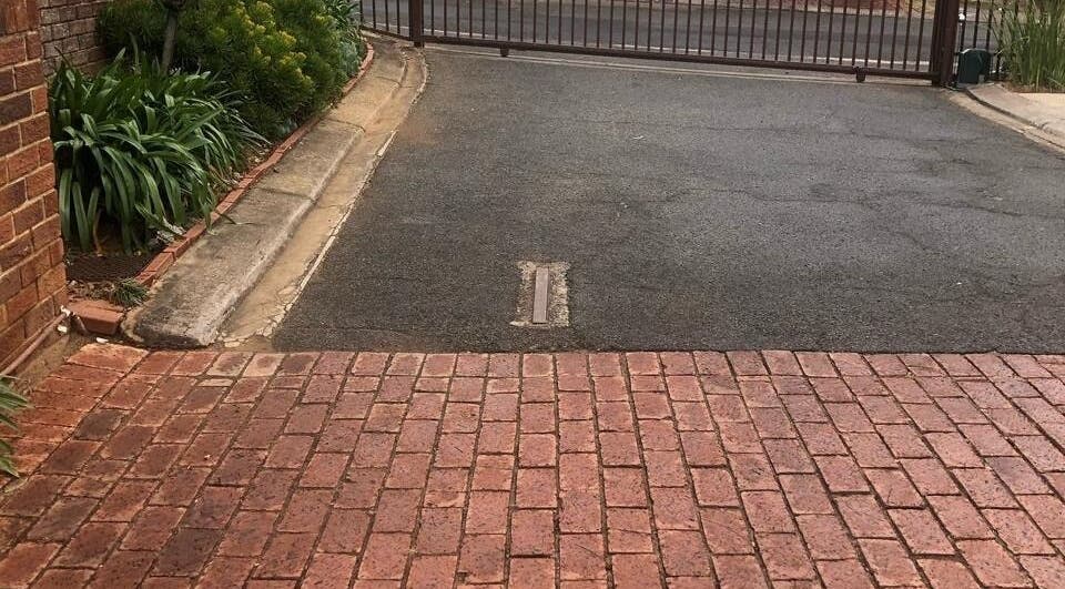 Entrance gate of Vuyo's Sanctuary in Sandton, Gauteng, ZA, surrounded by lush greenery and red brick path.