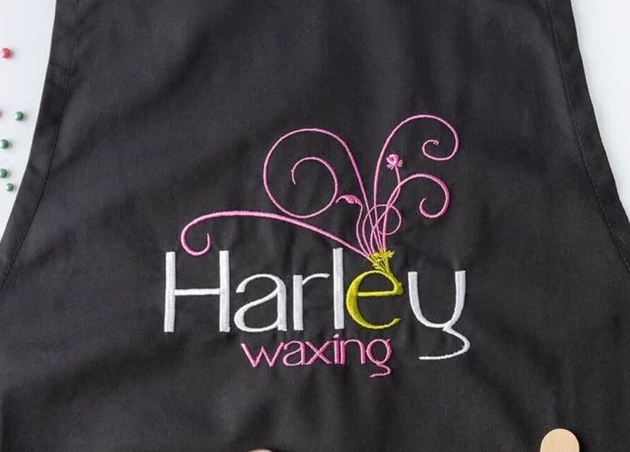 Studio M black apron with 'Harley waxing' embroidery, Lisnaskea, Northern Ireland, GB.
