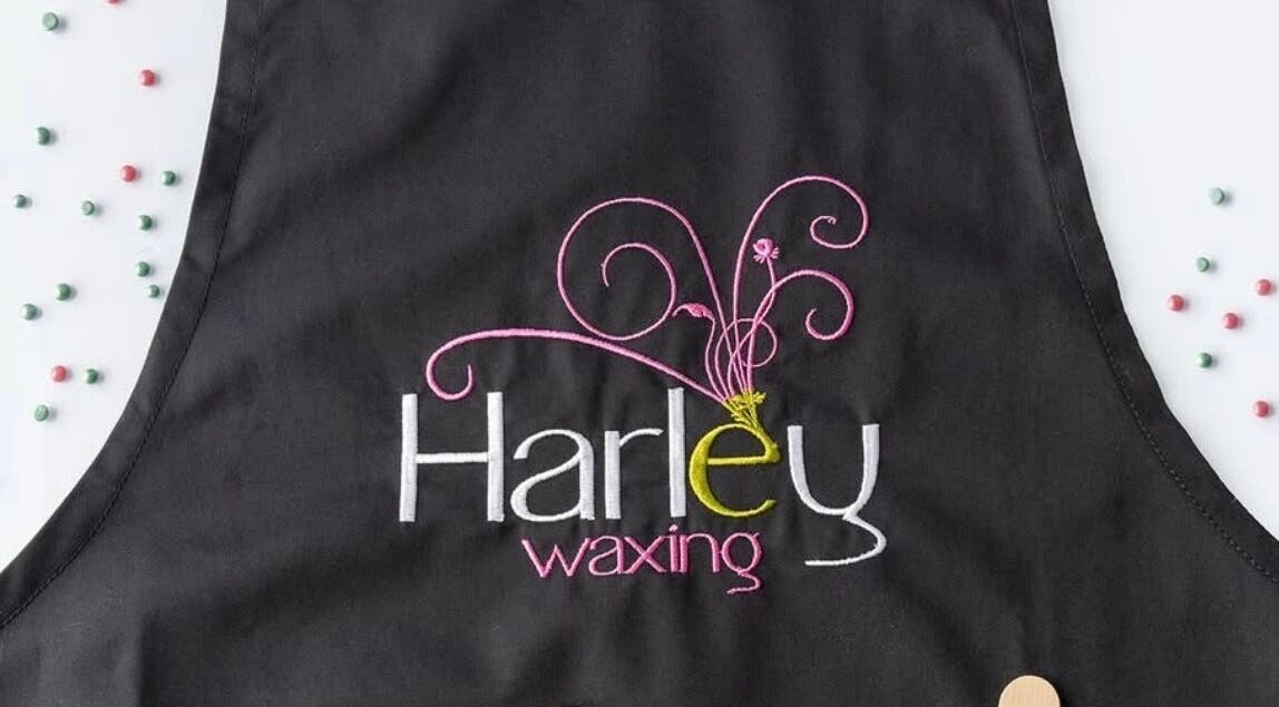 Studio M black apron with 'Harley waxing' embroidery, Lisnaskea, Northern Ireland, GB.
