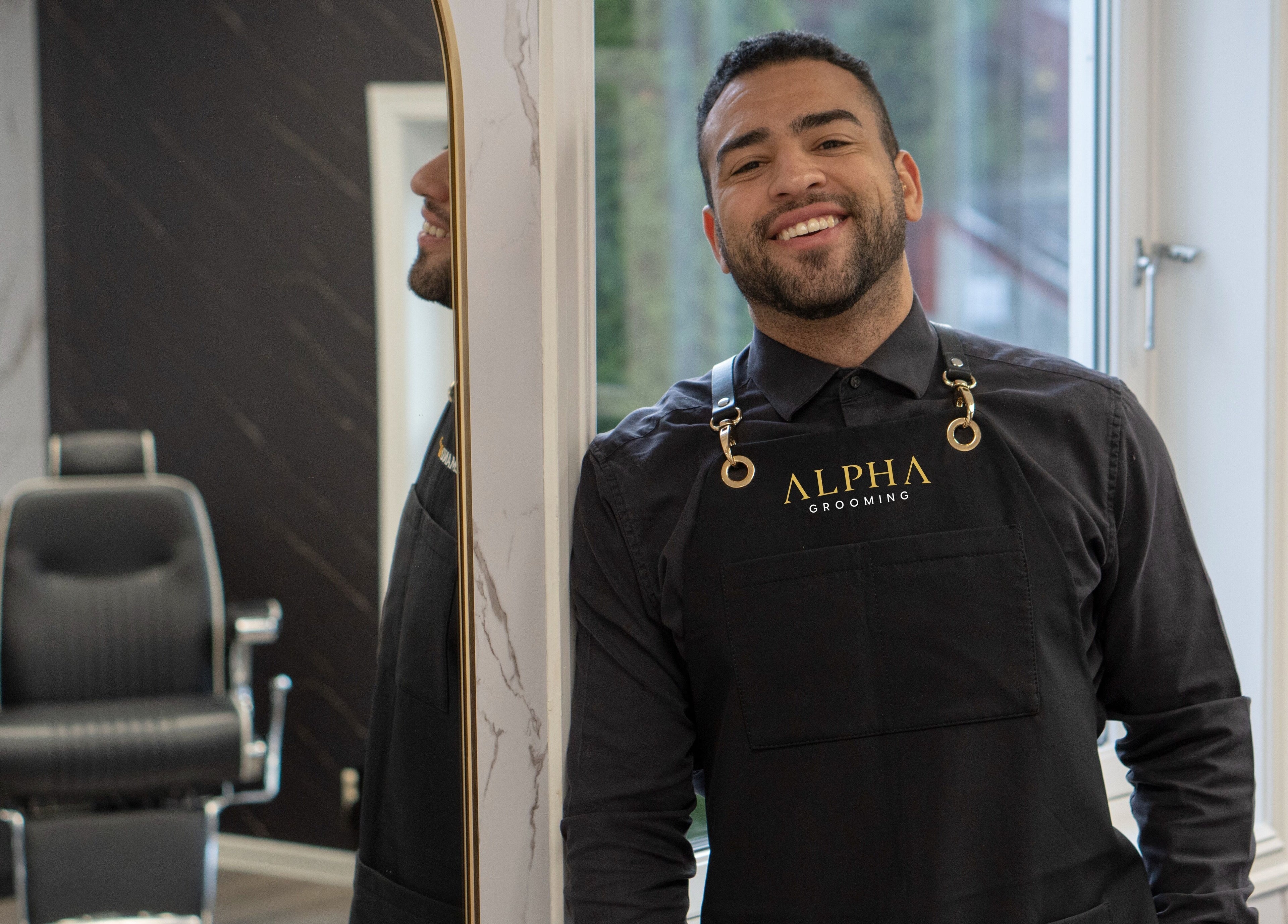 Ansatt i Alpha Grooming, Oslo, Oslo, NO, smiler foran en moderne herrefrisørsalong.