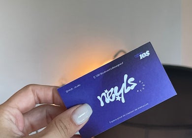 Carte de visite de Neyls Studio à Québec, Québec, CA, tenue par une main avec fond de bureau.
