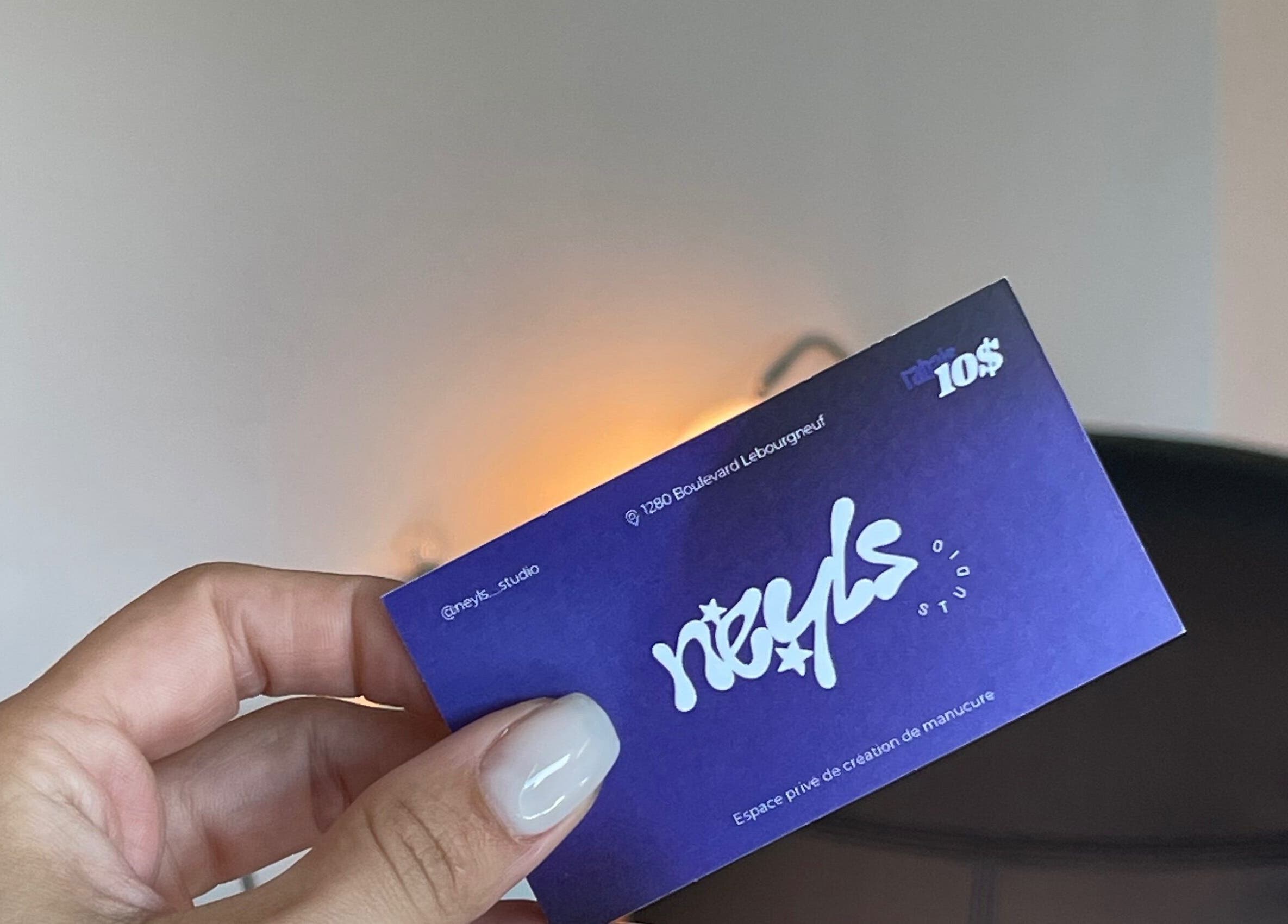 Carte de visite de Neyls Studio à Québec, Québec, CA, tenue par une main avec fond de bureau.