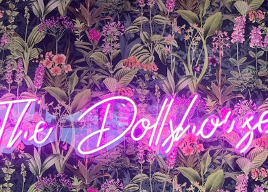 Vibrant neon sign of The Dollshouse Hair By Nat in Shortheath, England, with floral backdrop.