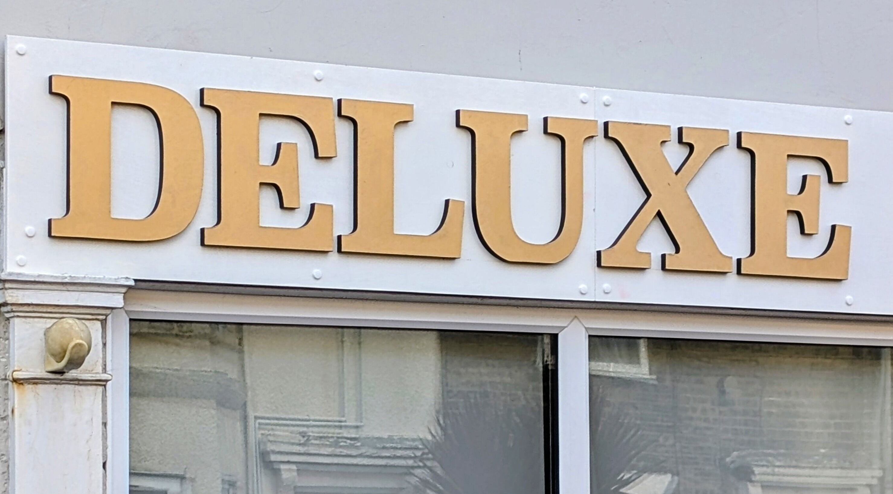Golden 'Deluxe' sign at Deluxe Hairdressers, Lowestoft, England, GB showcasing the venue entrance.
