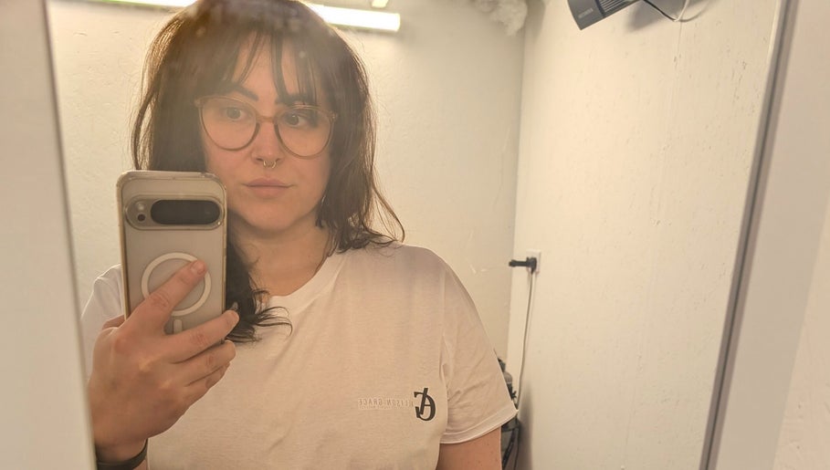 Person taking a mirror selfie at Allison Grace Sports Massage, Oldham, England, GB, wearing a branded shirt.