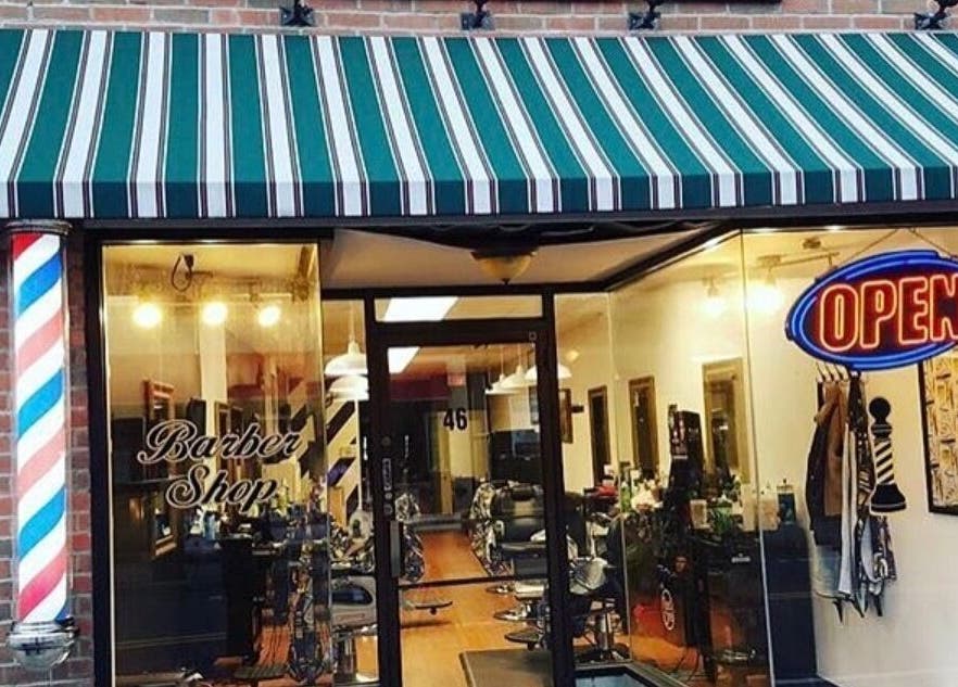 Front view of Luisthebarber-evolutionpatchogue in Patchogue, New York, US with striped awning and neon open sign.