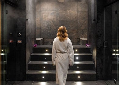 Mujer en bata blanca en spa relajante de Calma Spa, Tulum, Quintana Roo, MX, rodeada de velas y vapor.