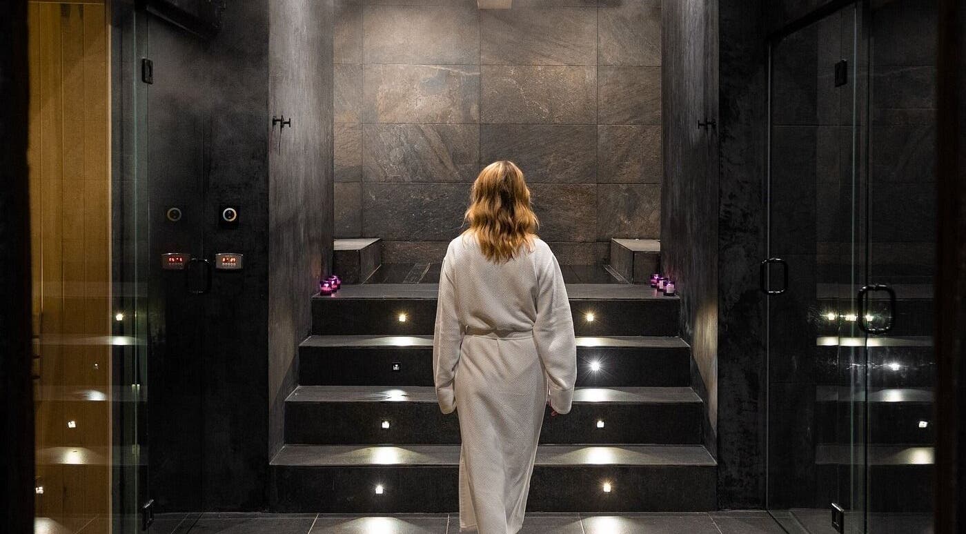 Mujer en bata blanca en spa relajante de Calma Spa, Tulum, Quintana Roo, MX, rodeada de velas y vapor.