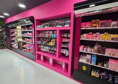 Ράφι με προϊόντα μακιγιάζ στο W7 Professional Make Up, Αχαρνες, GR με εντυπωσιακό ροζ ντεκόρ και φωτισμό.