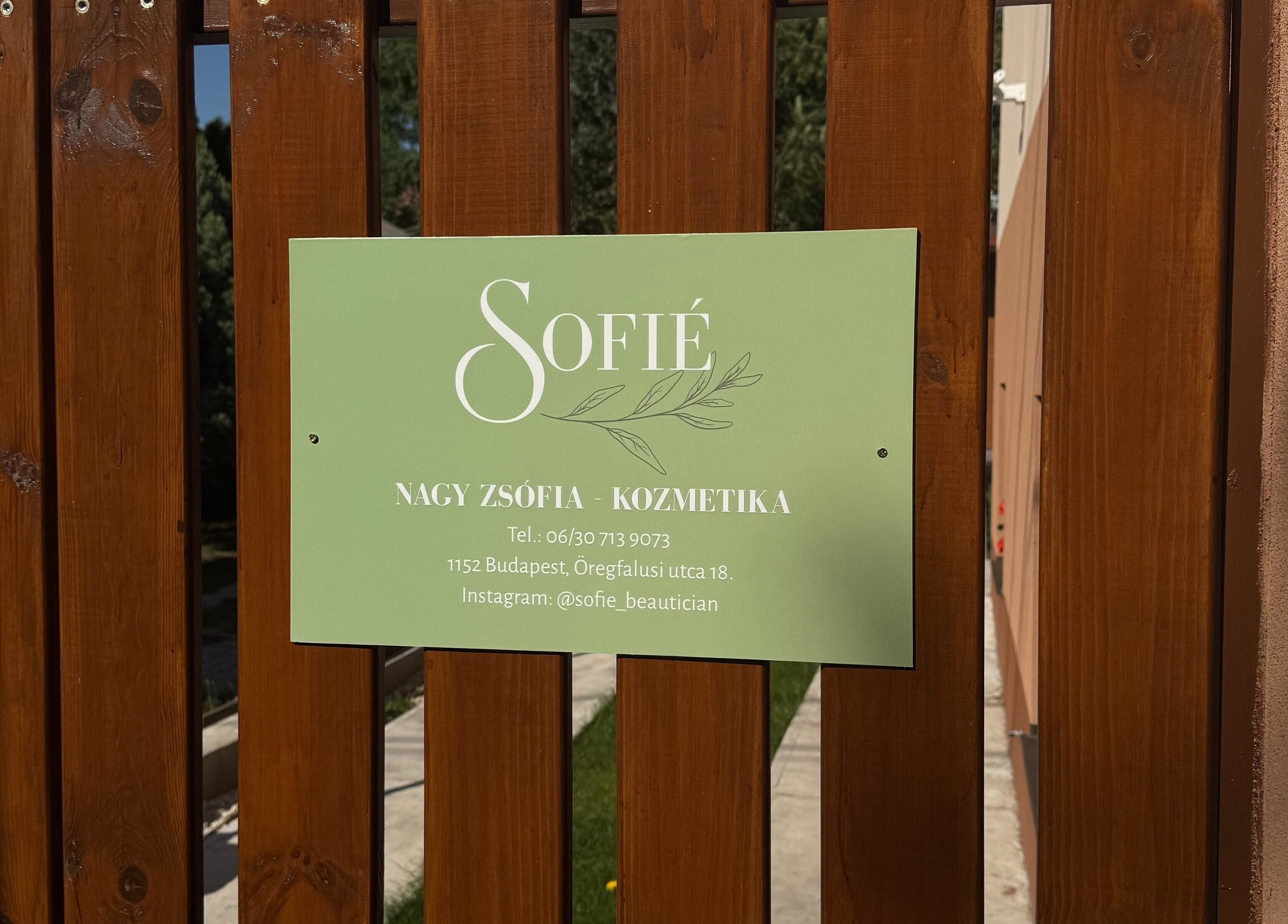 Sofié kozmetika zöld táblája egy fa kerítésen, Budapest, Magyar, HU című kozmetikai szalon előtt.