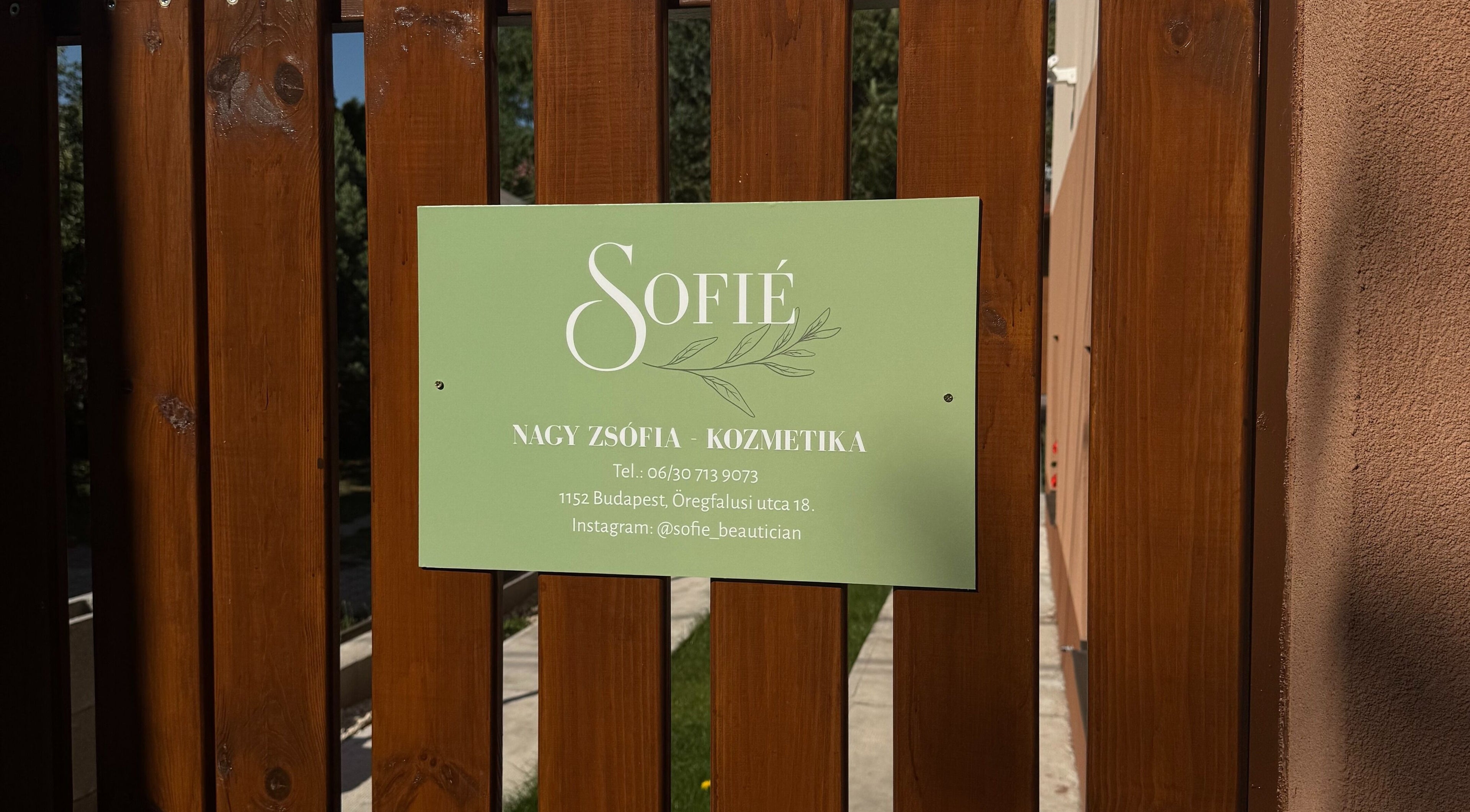 Sofié kozmetika zöld táblája egy fa kerítésen, Budapest, Magyar, HU című kozmetikai szalon előtt.