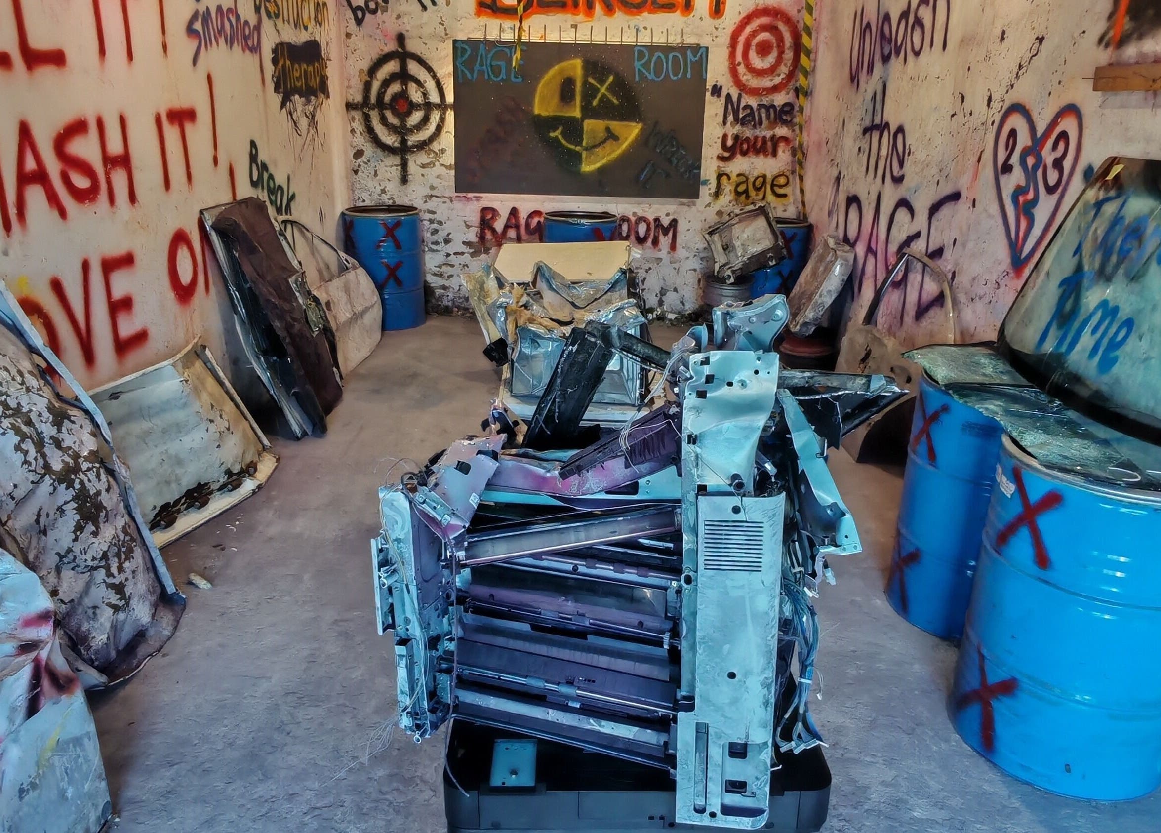 Interior view of Bliksem Rage Room, Gqeberha, Eastern Cape, ZA, showcasing creative wall graffiti and breakable items.