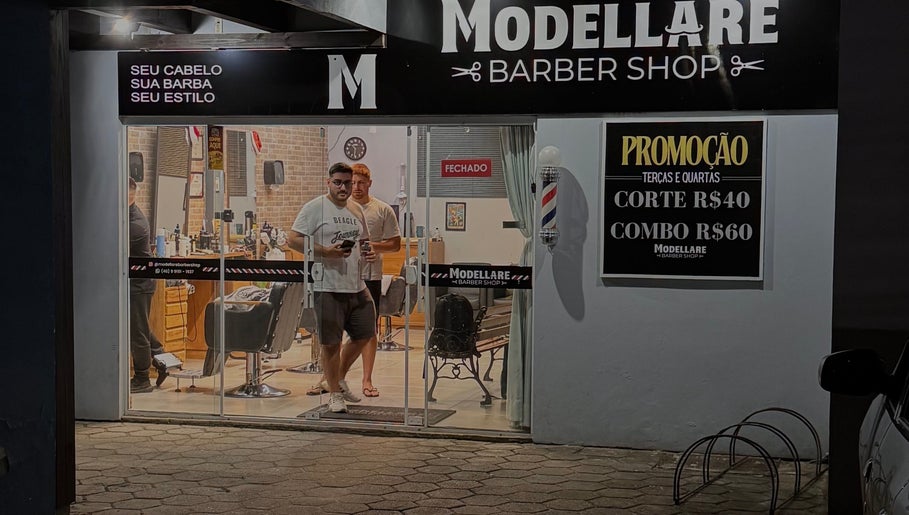 Entrada do Modellare Barbershop à noite, em Santa Catarina, BR, destacando cartões e ambiente moderno.