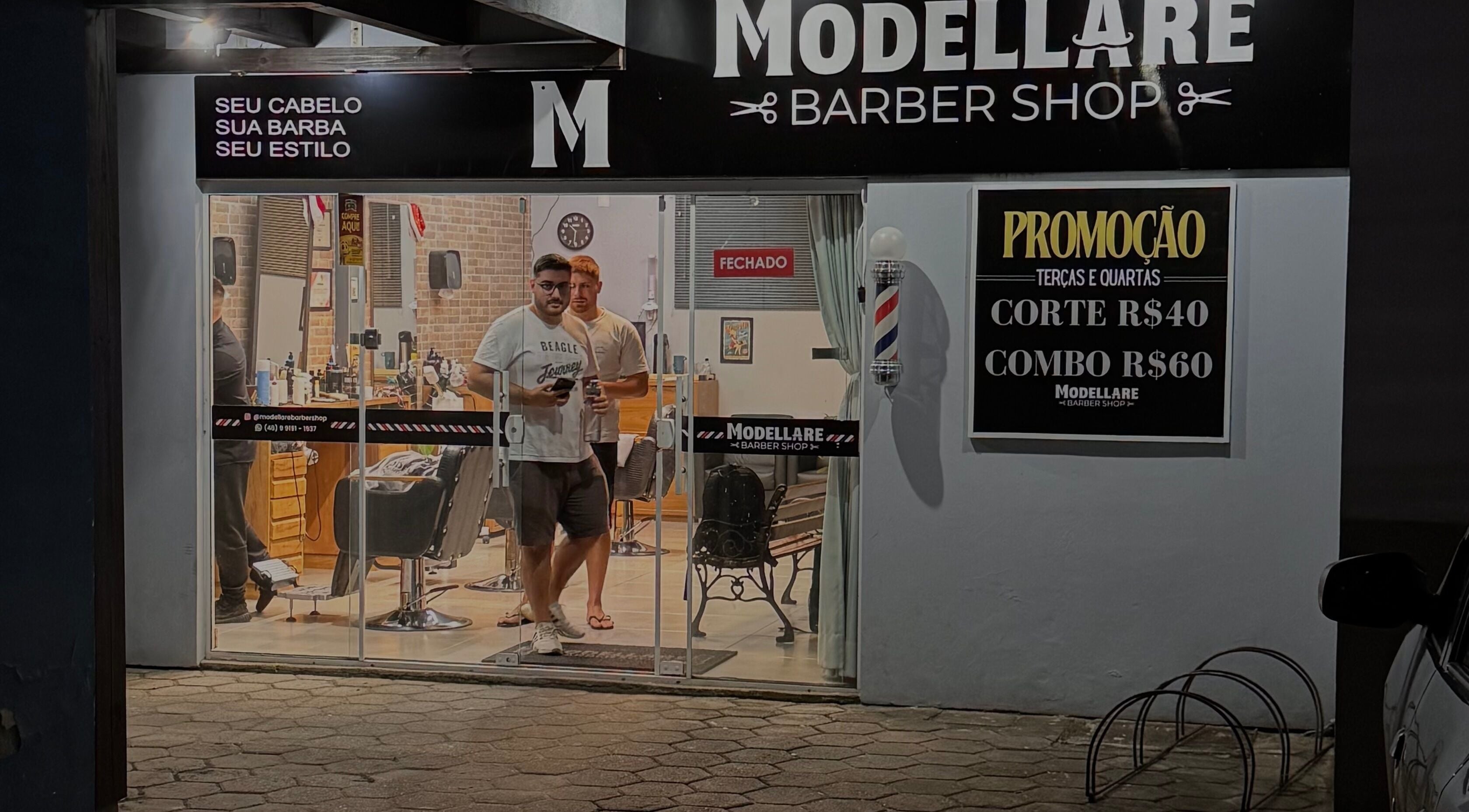 Entrada do Modellare Barbershop à noite, em Santa Catarina, BR, destacando cartões e ambiente moderno.
