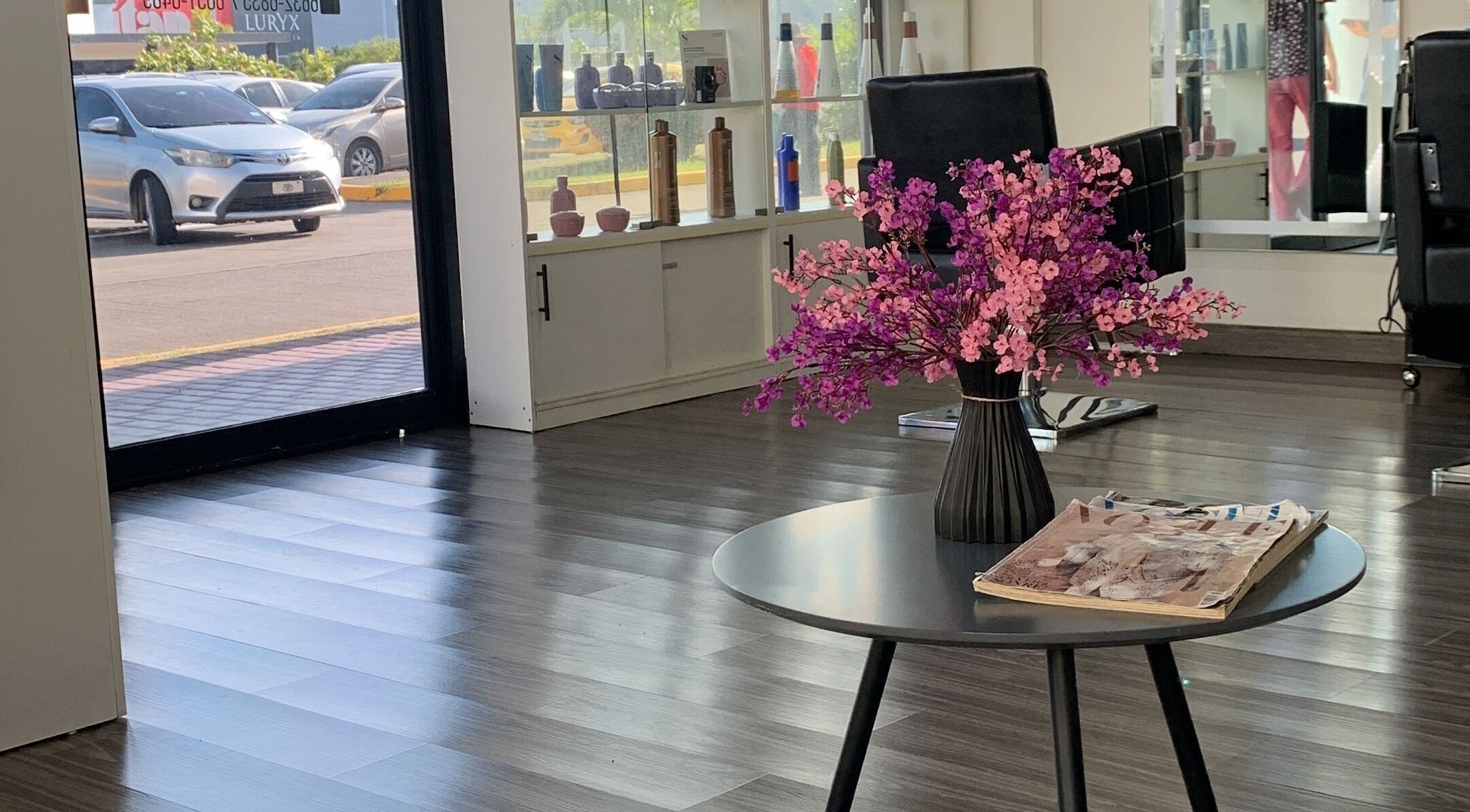 Interior elegante de Capilarium Los Pueblos, Panamá. Ramo de flores en mesa junto a sillas de salón de belleza.