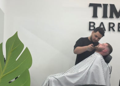 Barber styling a client's beard at TIMIJBARBERS in Paisley, Scotland, GB. Relaxing ambiance with greenery.