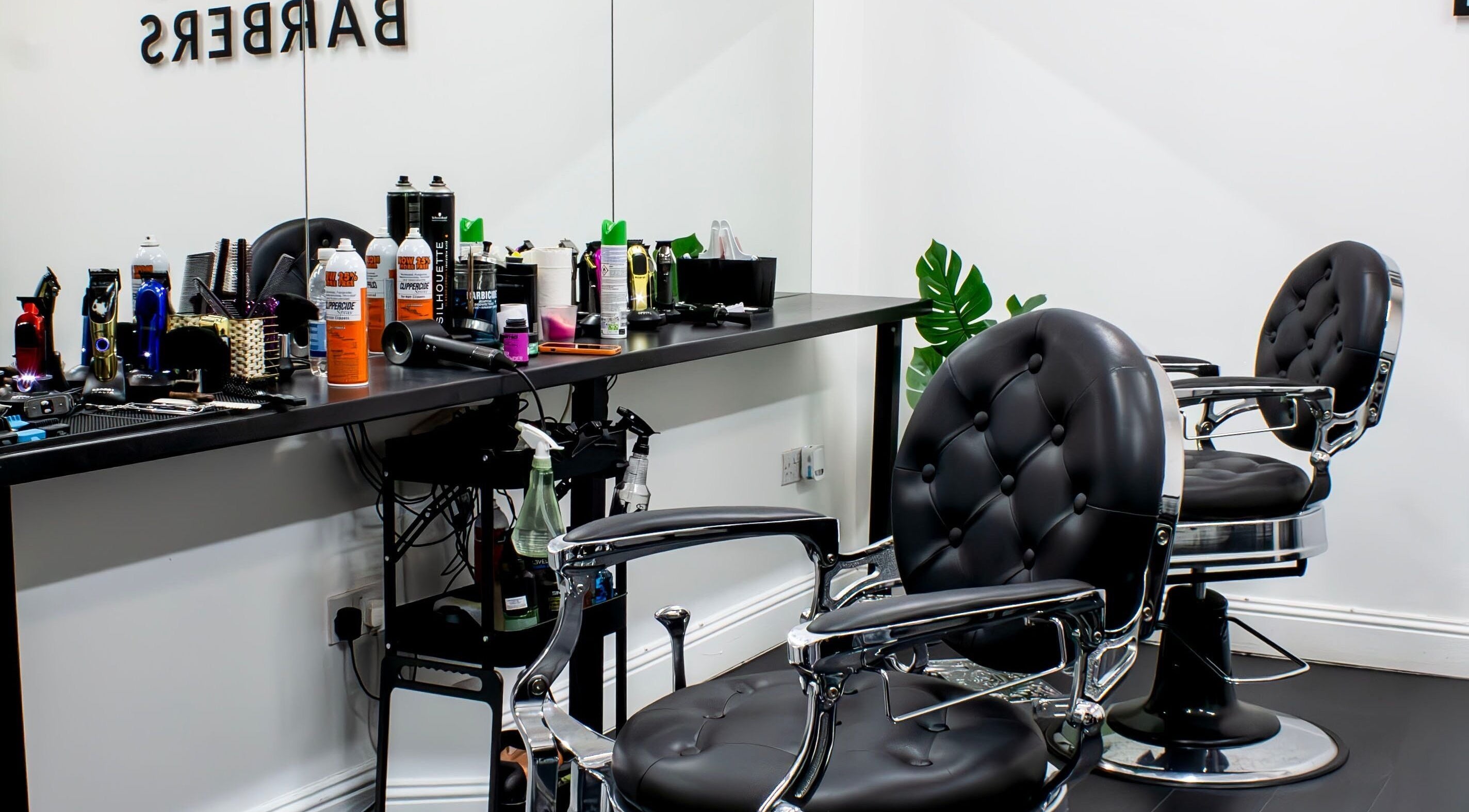 Modern barbershop interior at TIMIJBARBERS, Paisley, Scotland, GB, featuring stylish black chairs and grooming tools.