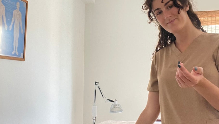 Terapeuta sorridente em Corpus Curatio, São João Da Madeira, Aveiro, PT, em frente a uma mesa de tratamento.