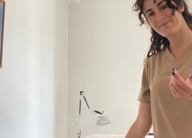 Terapeuta sorridente em Corpus Curatio, São João Da Madeira, Aveiro, PT, em frente a uma mesa de tratamento.
