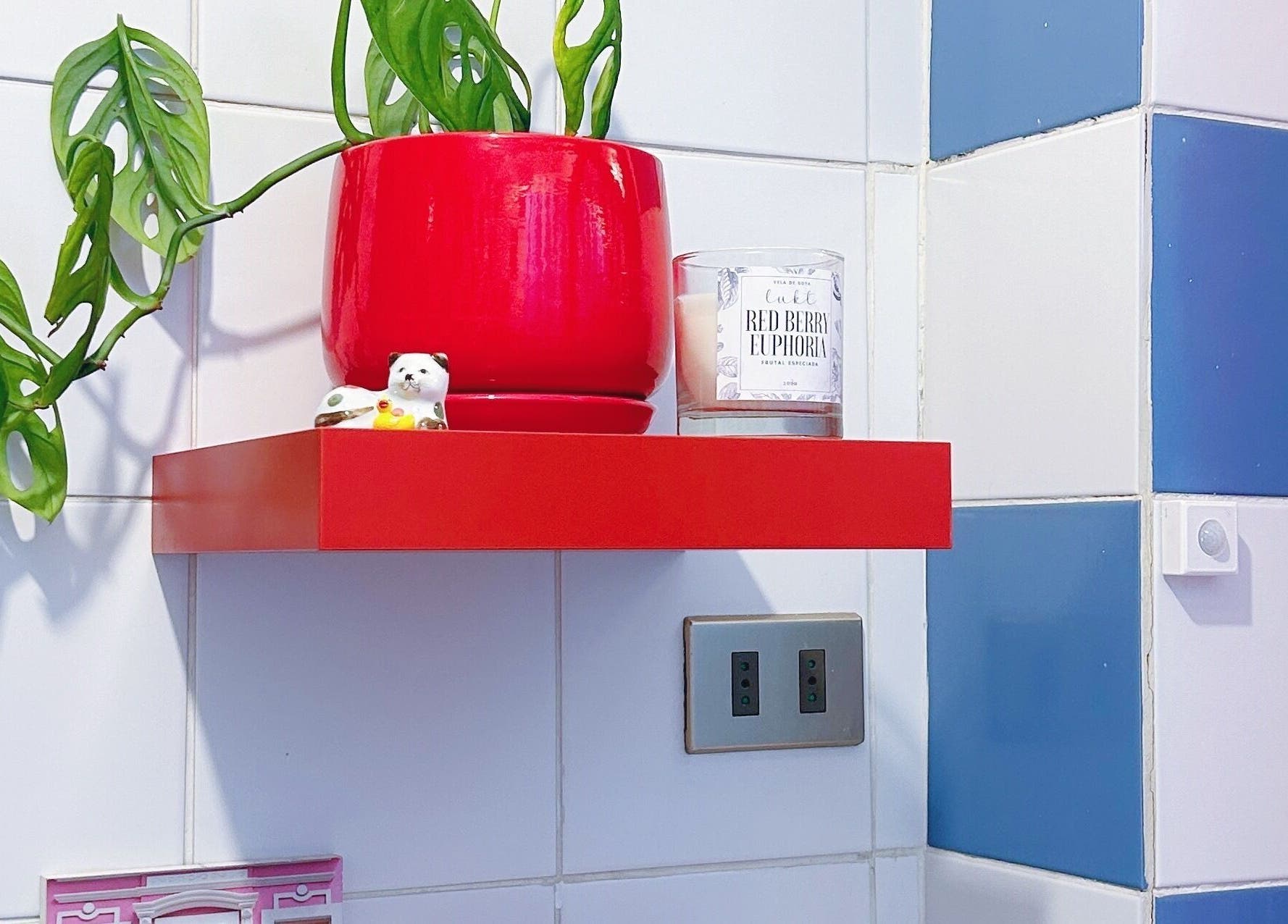 Estante rojo en palasgatasgarras, Providencia, con planta y vela decorativa sobre azulejos blancos y azules.